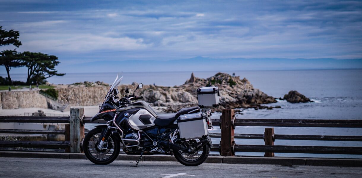 Motorrad mit Hecktaschen steht an einer Straße, Meer im Hintergrund.