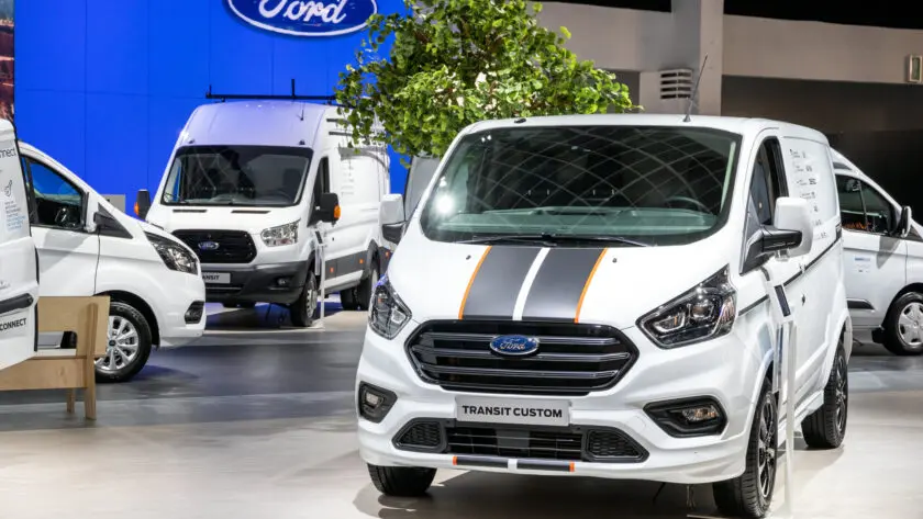 Mehrere Ford Transit Custom Modelle auf einer Automobilausstellung, im Vordergrund ein weißer Transit Custom mit sportlichen Streifen.