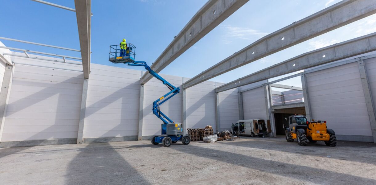 Arbeiter auf blauer Arbeitsbühne in Industriehalle bei Aufbauarbeiten