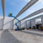 Arbeiter auf blauer Arbeitsbühne in Industriehalle bei Aufbauarbeiten