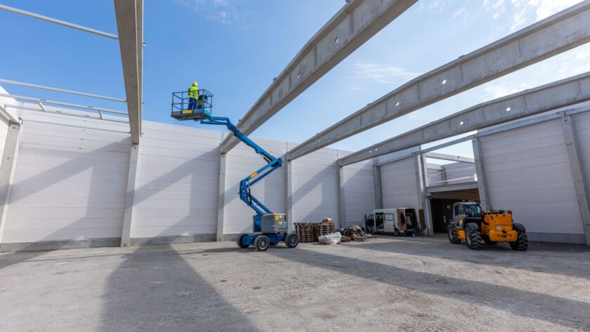 Arbeiter auf blauer Arbeitsbühne in Industriehalle bei Aufbauarbeiten